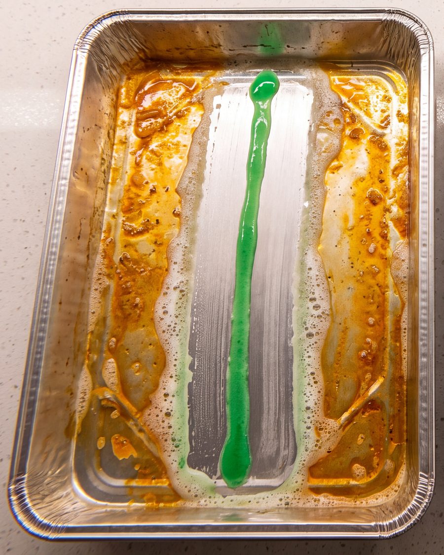 A greasy pan with one long line of dish soap cutting a clean strip