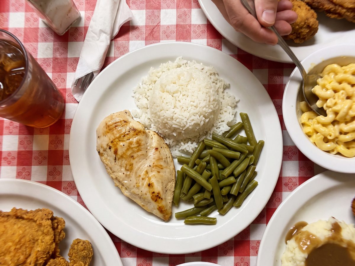 A plain plate of chicken, rice and green beans among plates of fried chicken